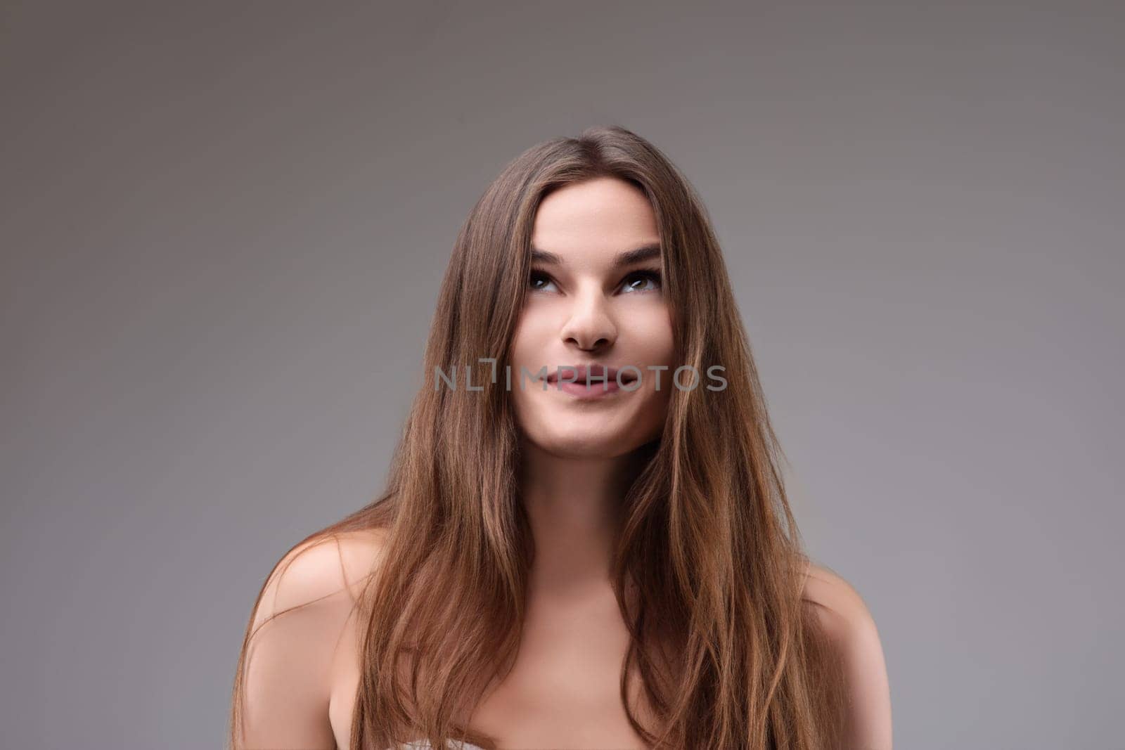 Young woman with long brown hair gazes up thoughtfully, radiating happiness and positivity in a studio portrait