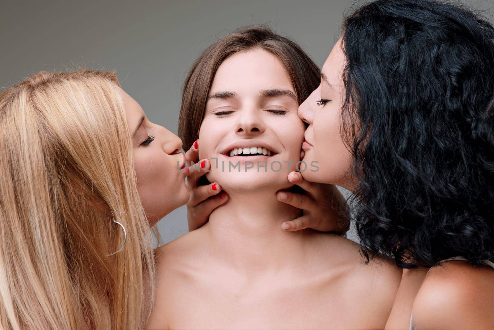 Three women affectionately kiss a young girl, all smiling with red nail polish and blond hair, showing love in a tender moment of friendship