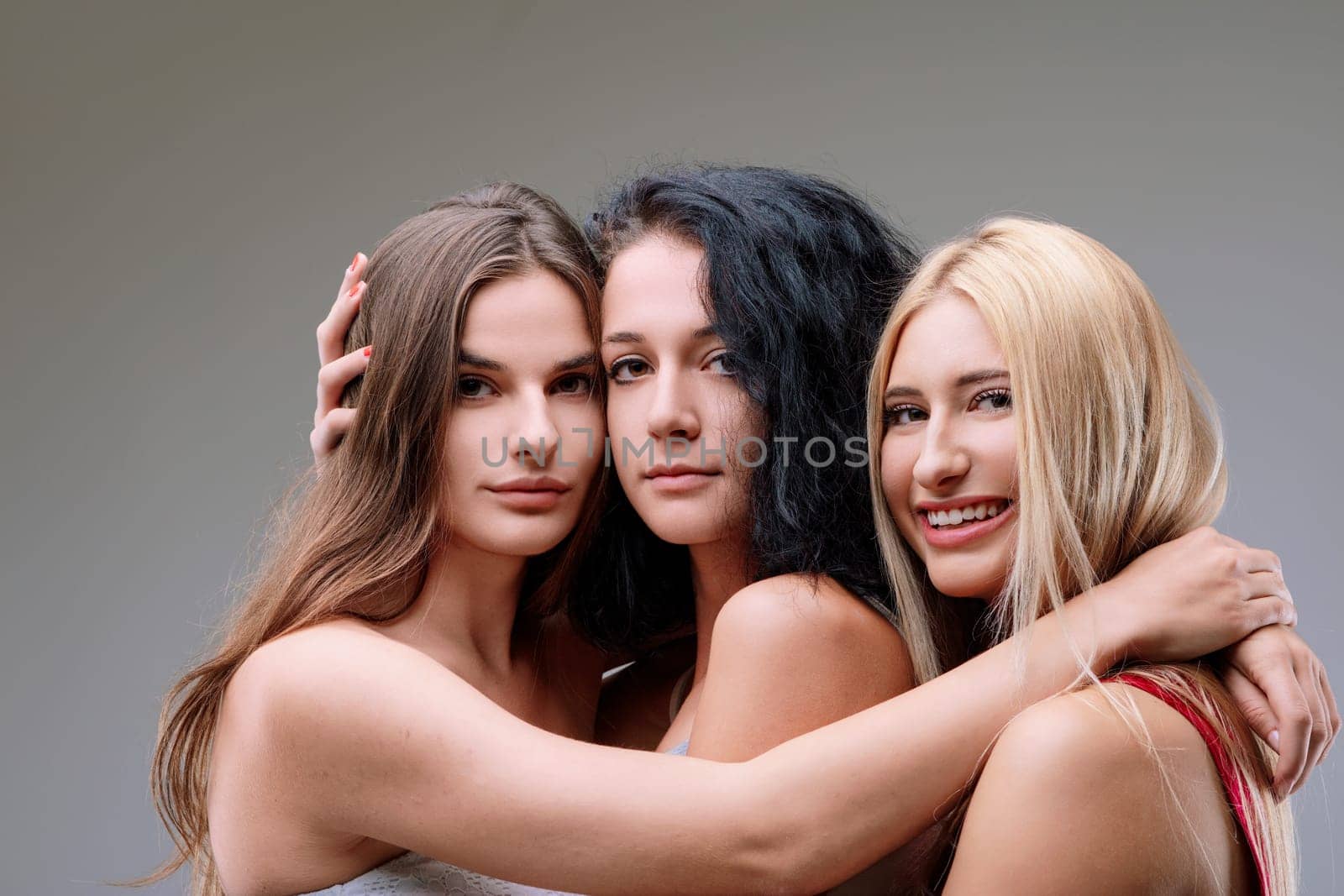 Three beautiful young women embrace tightly, radiating happiness and affection, showcasing the power of unity and support among females in a heartwarming studio shot