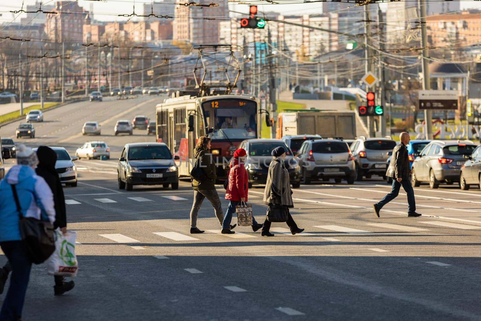 pedestrians crossing road in front of cityscape at sunny morning in Tula, Russia - October 23, 2021