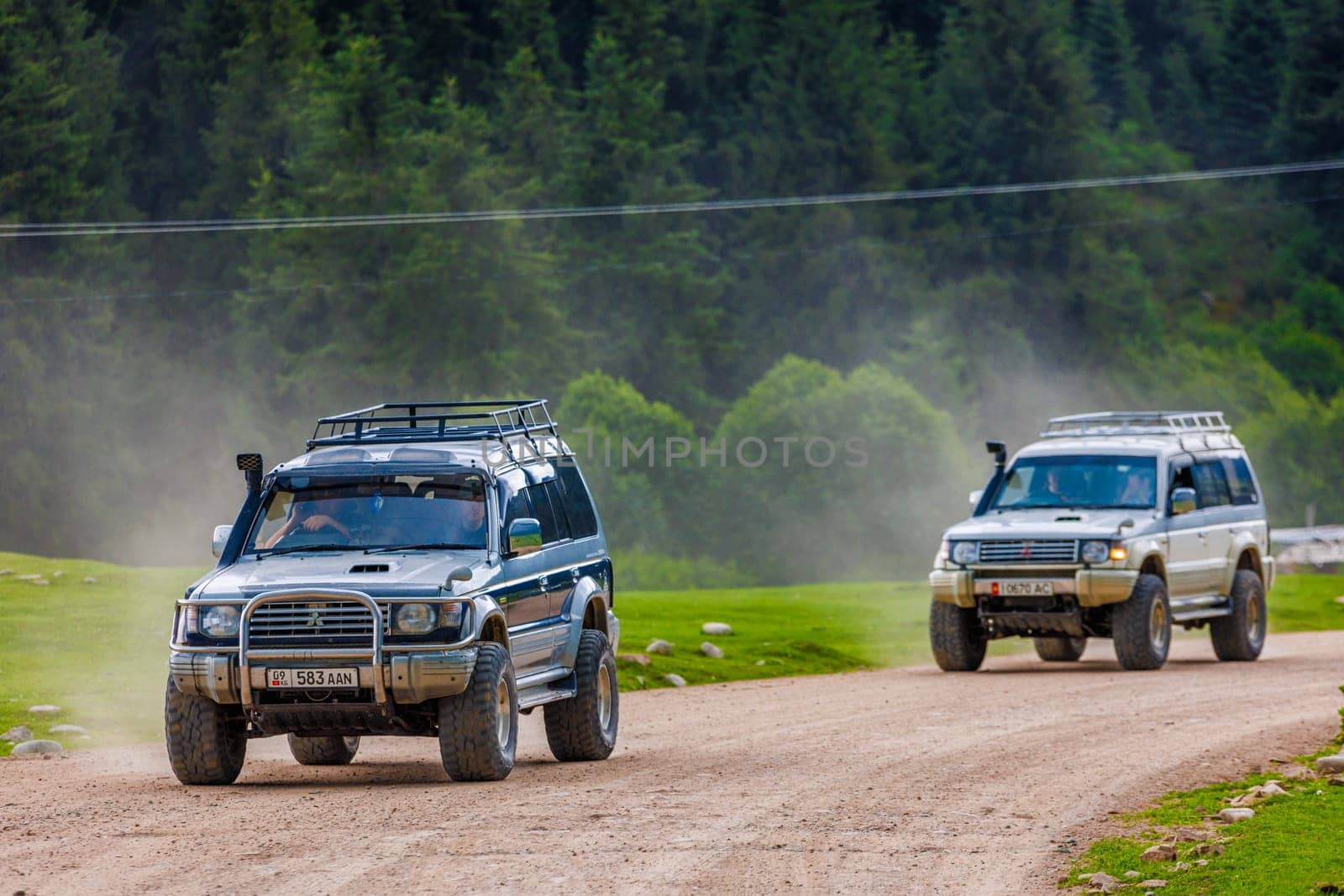 Two SUVs on rugged forest road, leaving dusty paths, symbolizing adventure and exploration in nature in Semenovskoye gorge, Kyrgyzstan at July 5, 2023