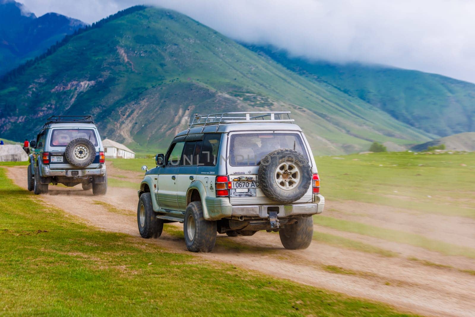 Two old SUVs on rugged mountain ravine road, leaving dusty paths, symbolizing adventure and exploration in nature in Semenovskoye gorge, Kyrgyzstan at July 5, 2023
