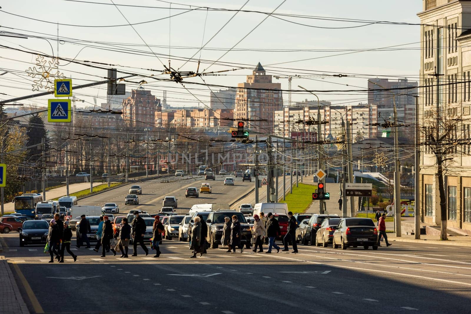 pedestrians crossing road in front of cityscape at sunny morning in Tula, Russia - October 23, 2021