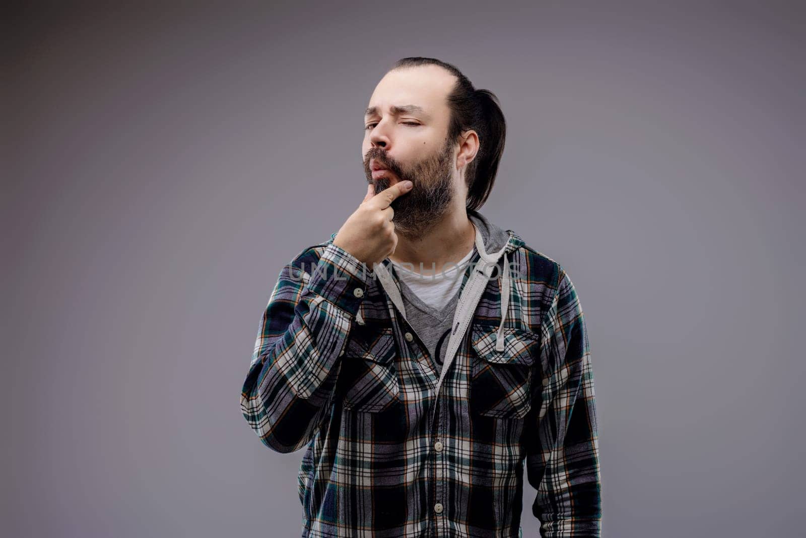 Young man deep in thought, touching his beard, looking uncertain and contemplative in a studio shot
