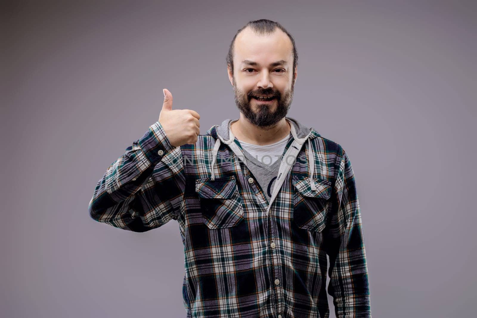 Bearded man in a green plaid shirt smiles and gives a thumbs up, radiating positivity and confidence. Perfect for conveying success and approval