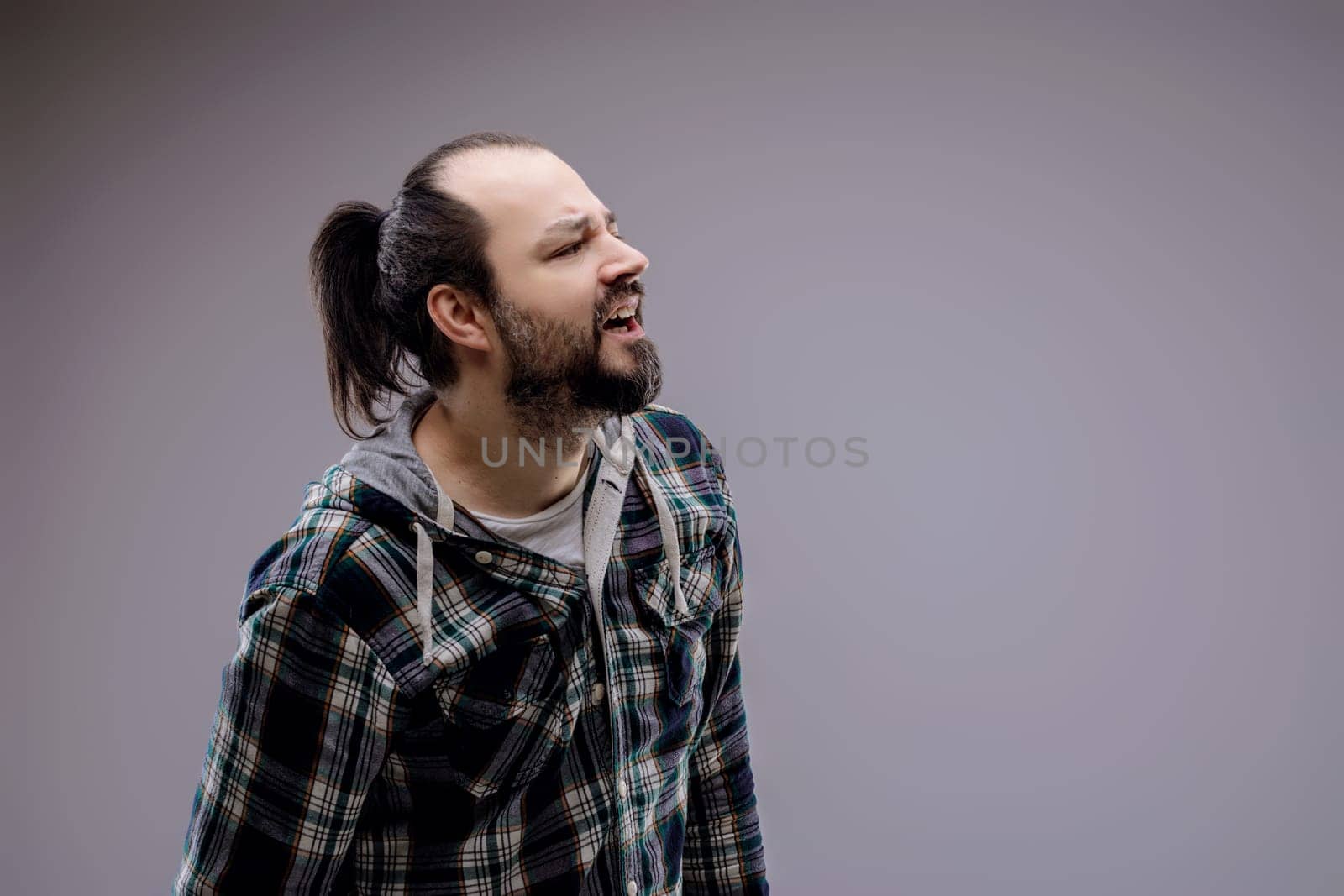 Young man with a beard and ponytail grimaces in pain, looking up and to the side, showing discomfort and agony