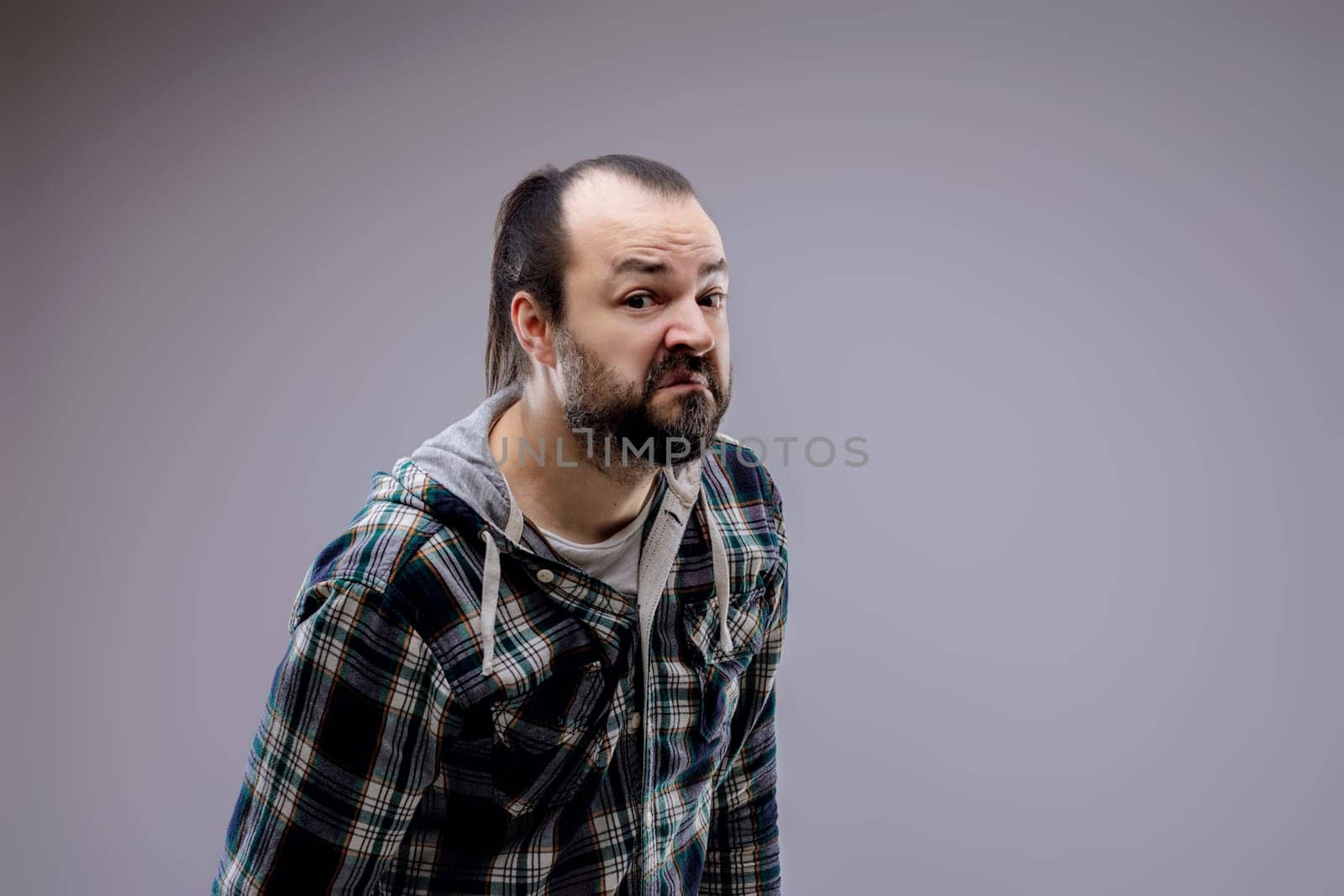 Bearded man in a checkered shirt makes a funny, skeptical face, showing confusion and humor