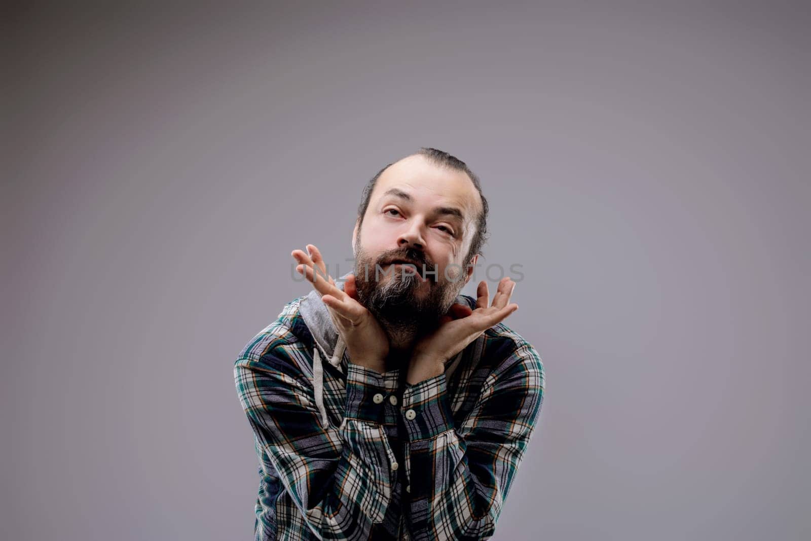 Stylish man with beard in studio, deep in thought, hands on face, curious expression, trendy portrait with copy space