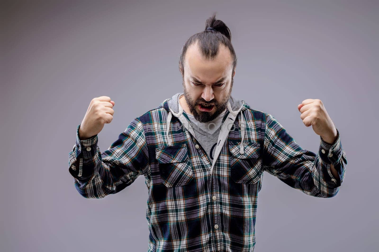 Bearded man with clenched fists expressing anger and frustration, studio shot on gray background. His expression and body language show a very upset person