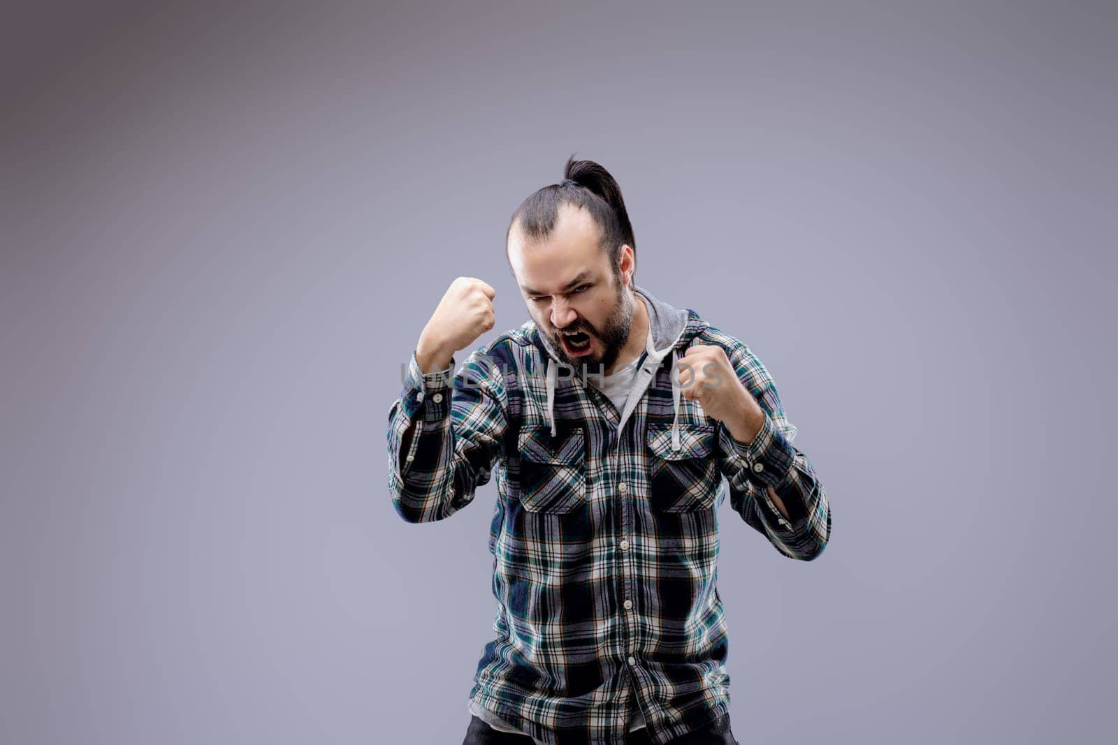 Young man is expressing negative emotions with an intense expression on his face, clenching his fists and opening his mouth wide