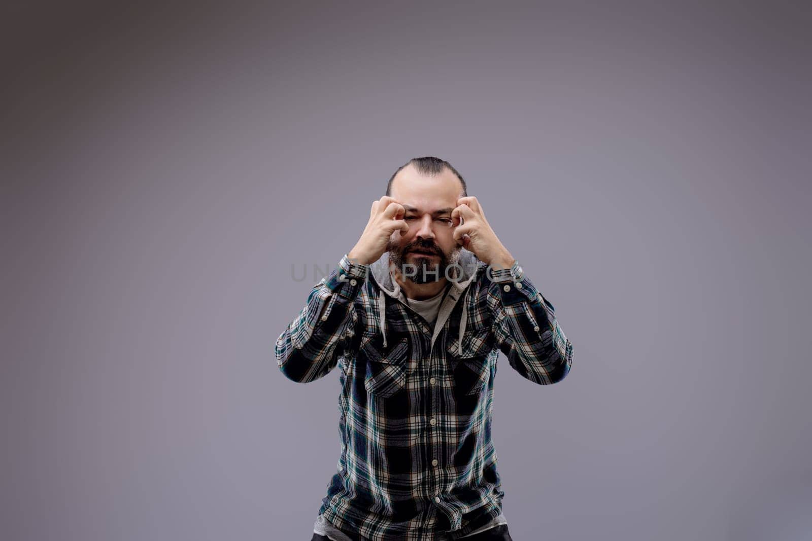Tired man with a beard rubs his eyes, showing fatigue and frustration, against a neutral gray background with space for text