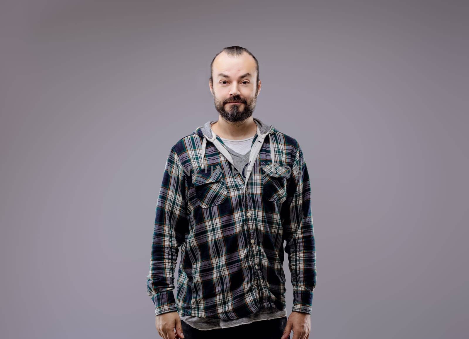 Confident man in plaid shirt standing against grey background, conveying seriousness and thoughtfulness. Shows healthy lifestyle and casual style