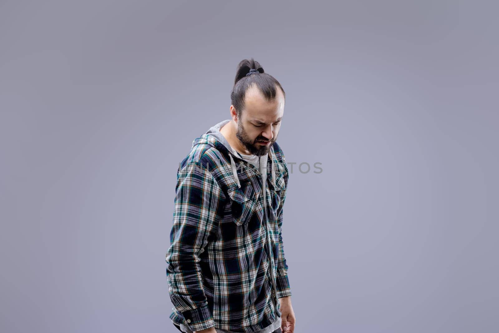 Man with a beard and a man bun looks down, showing pain and discomfort. His sad expression reflects backache, highlighting the need for healthcare