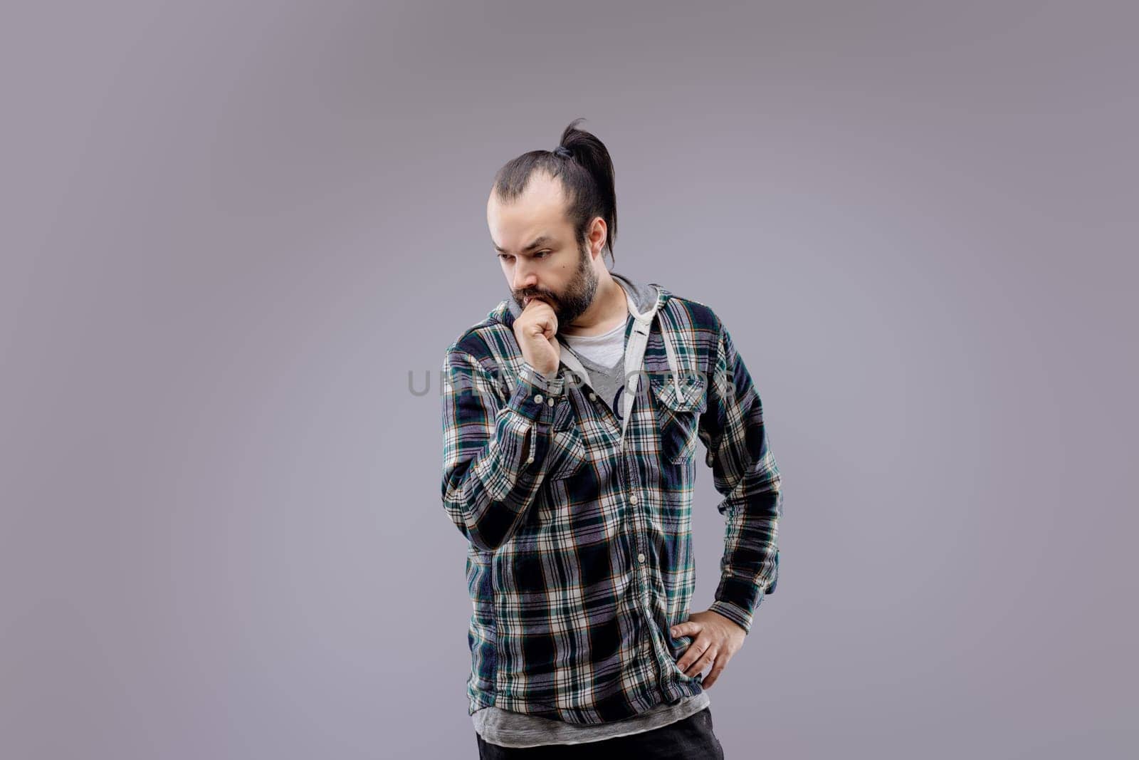 Bearded man with a ponytail is deep in thought, touching his beard as he contemplates something with a serious expression