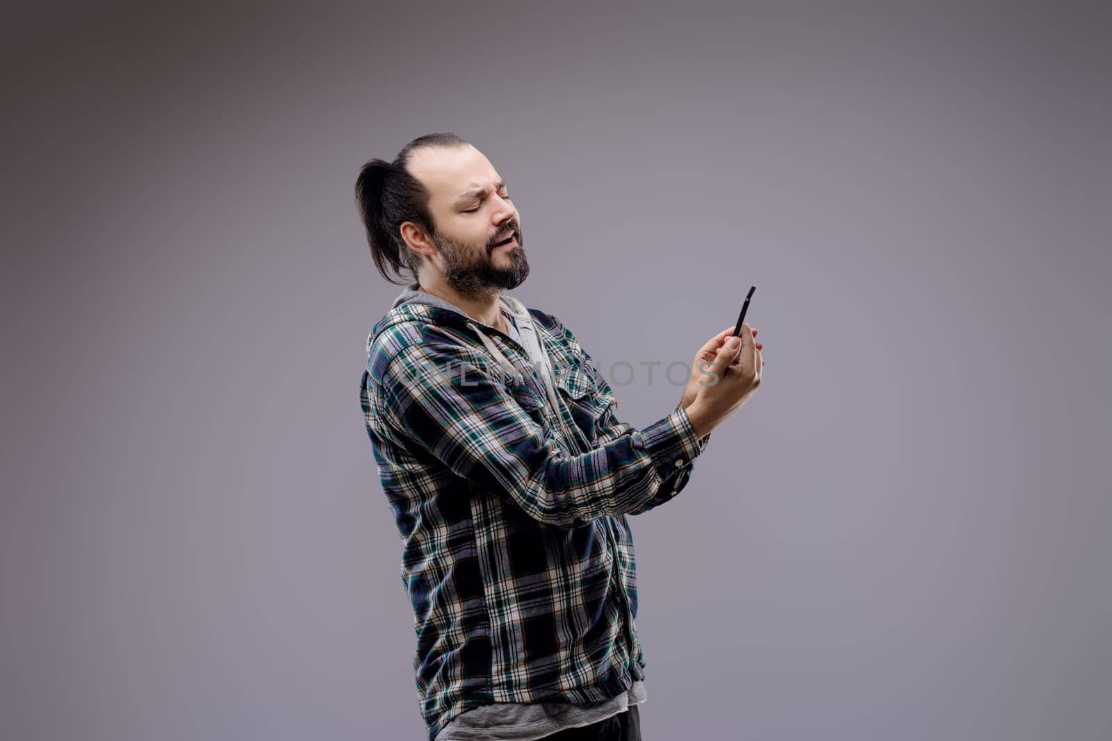 Man in his 30s, looking unhappy, reading bad news on his smartphone against a gray background