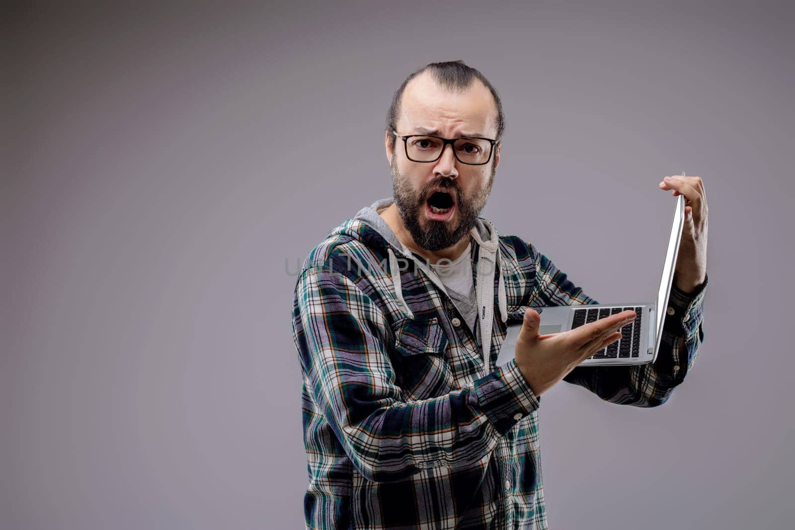 Frustrated technician screaming and holding laptop, overwhelmed by technology issues like errors, glitches, and viruses