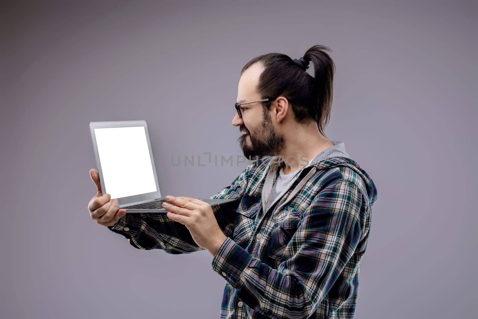 Concerned computer technician troubleshoots a laptop with a blank screen, showing worry and frustration in a gray studio