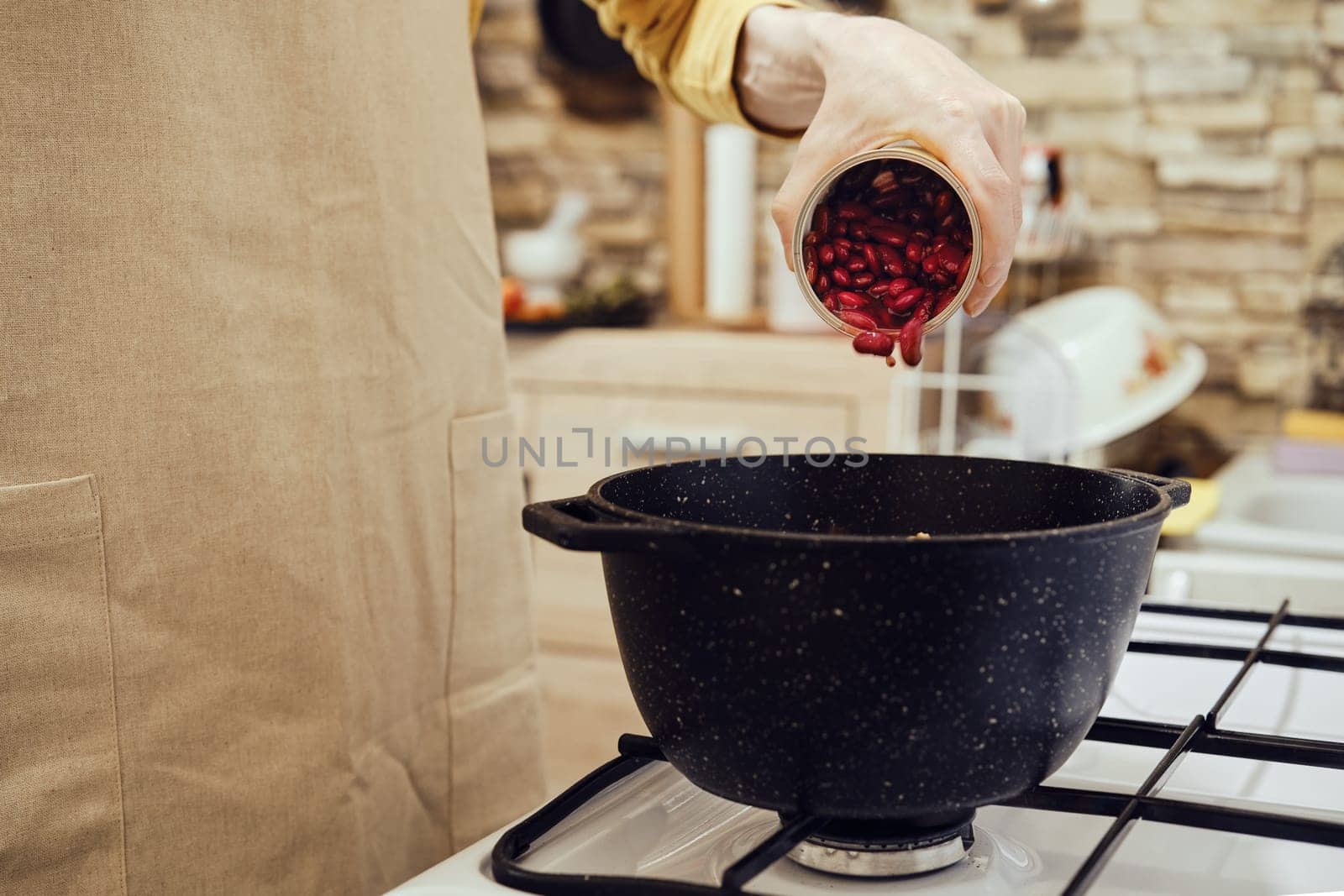 Unrecognizable man pours canned beans from tin can into a saucepan on a gas stove
