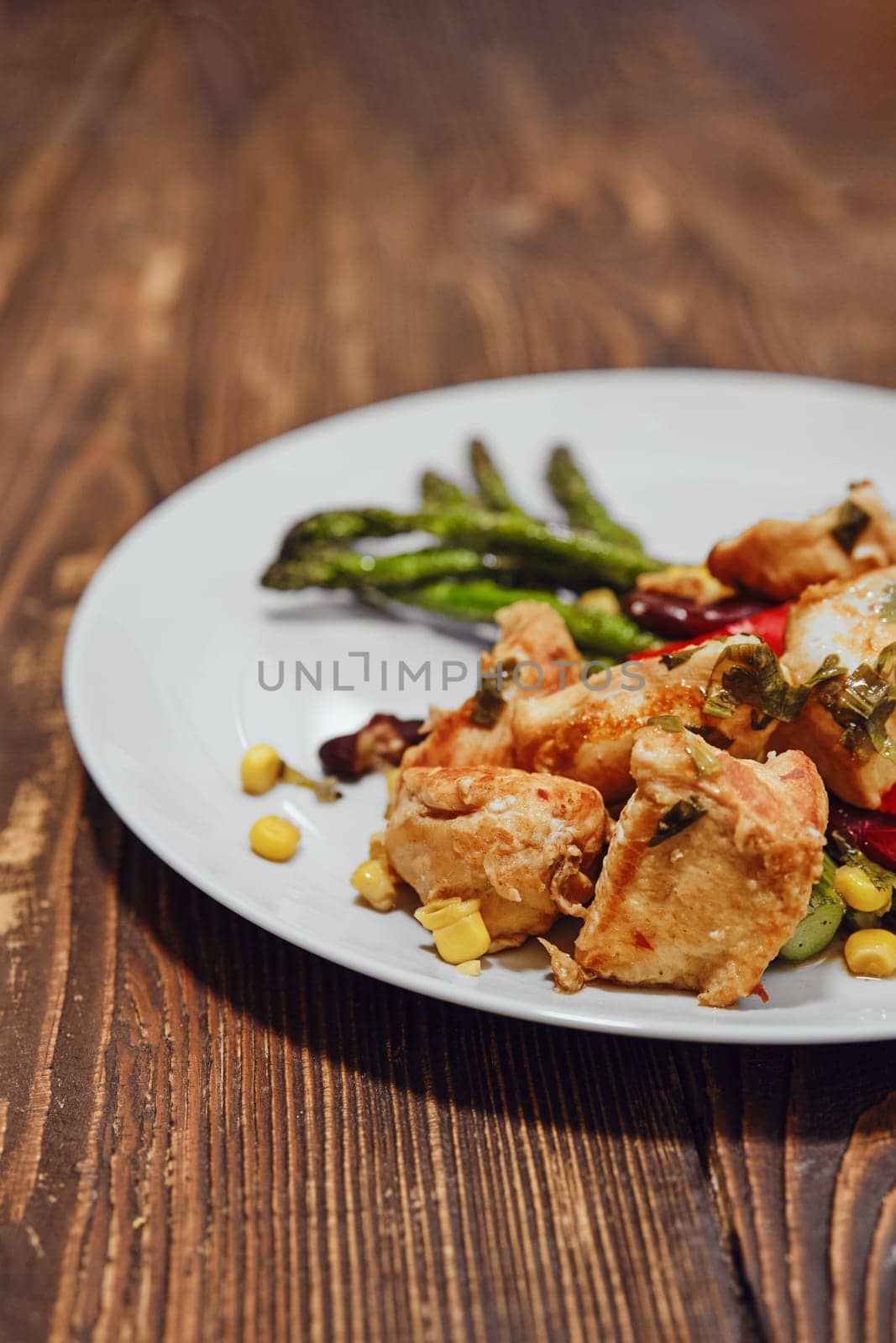 Close-up view of spicy chicken ragout with vegetables and fried asparagus on wooden background