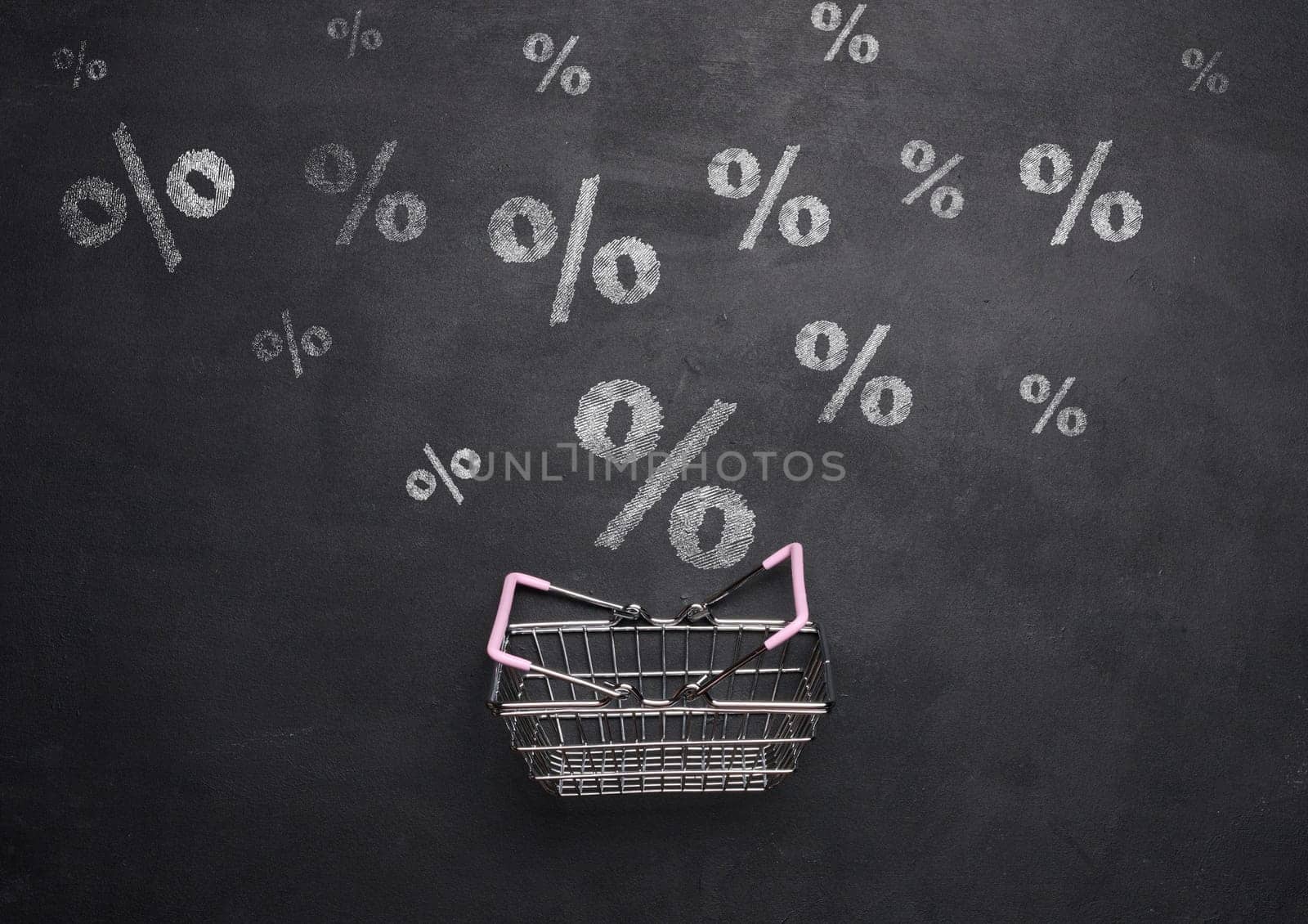 Miniature shopping metal cart on a background of a black chalk board with drawn percentages, discount start concept