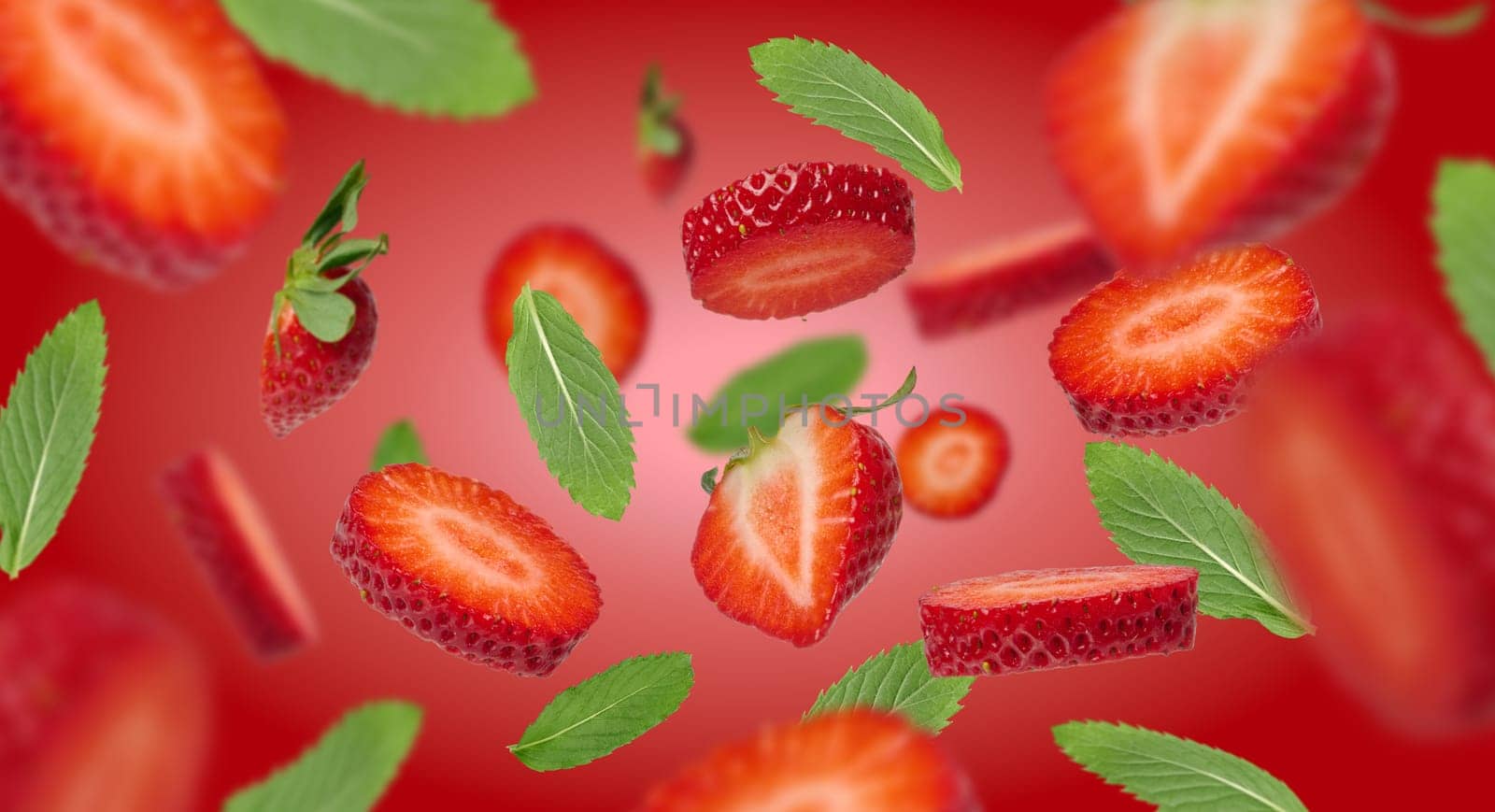 Pieces of ripe strawberries with green mint leaves levitate on a red background