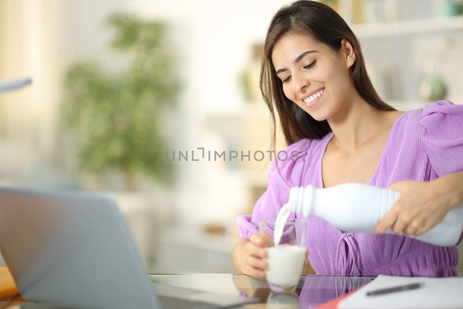 Happy student filling glass of milk e-learning at home