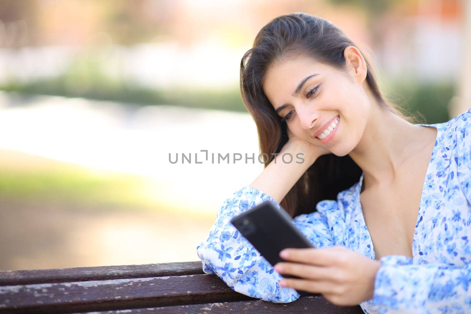 Happy female sitting on a bench reading phone message