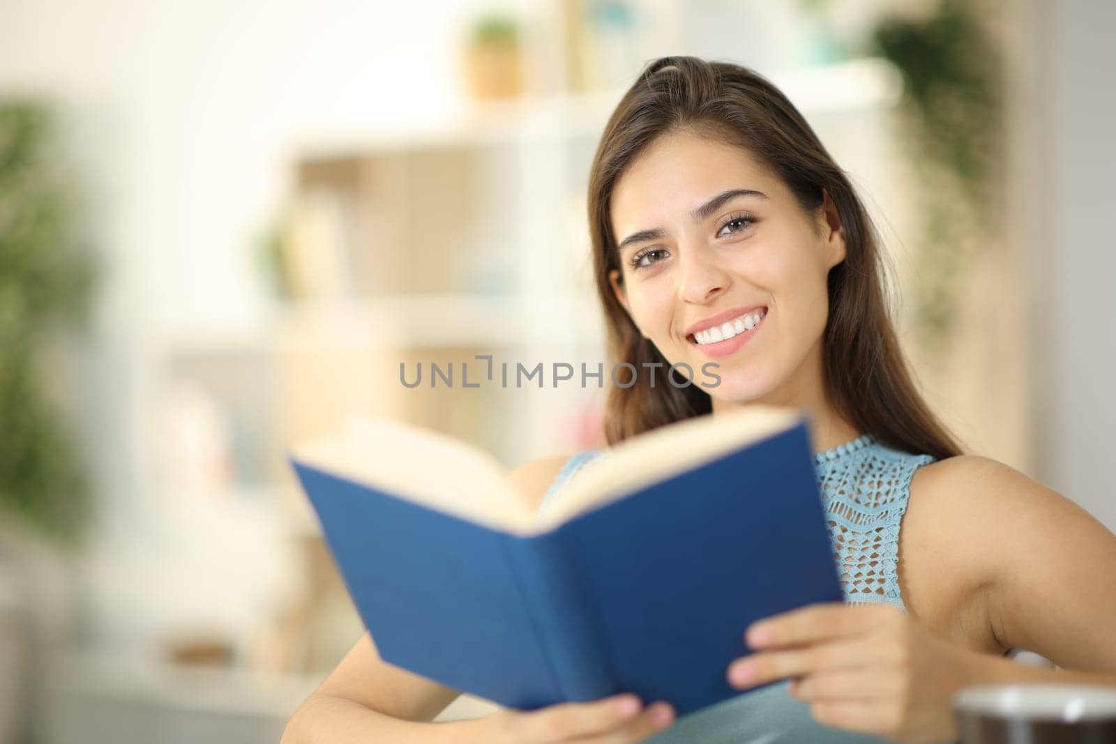 Portrait of a happy woman holding a book looking at you at home