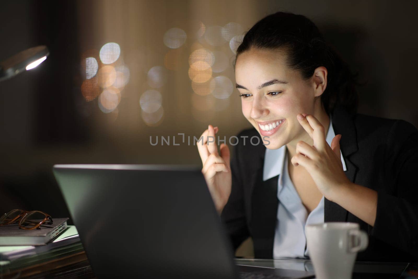 Happy executive working in the night crossing fingers checking laptop
