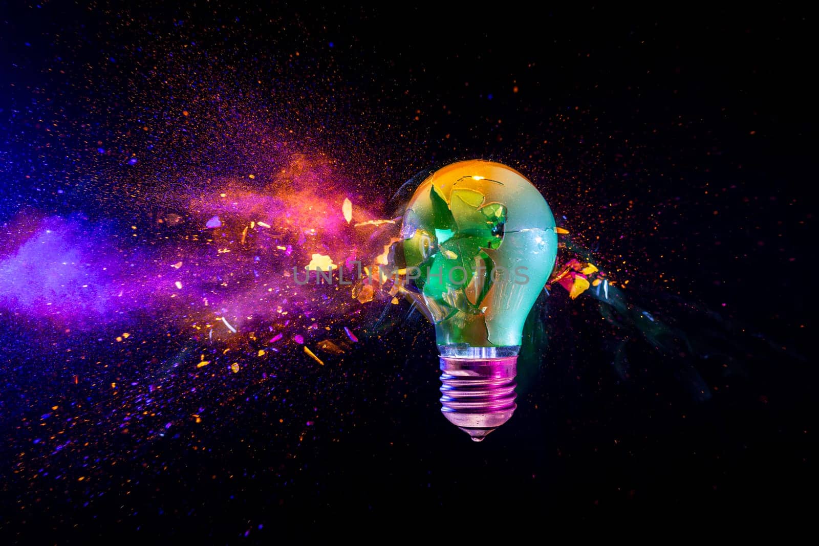 Broken light bulb exploding with colorful powder on a black background