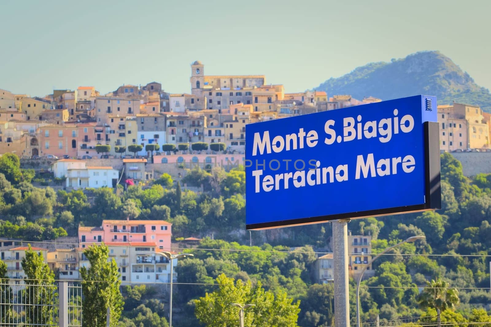 Signboard of the Monte San Biagio / Terracina Mare train station in Italy, with the town in the background.