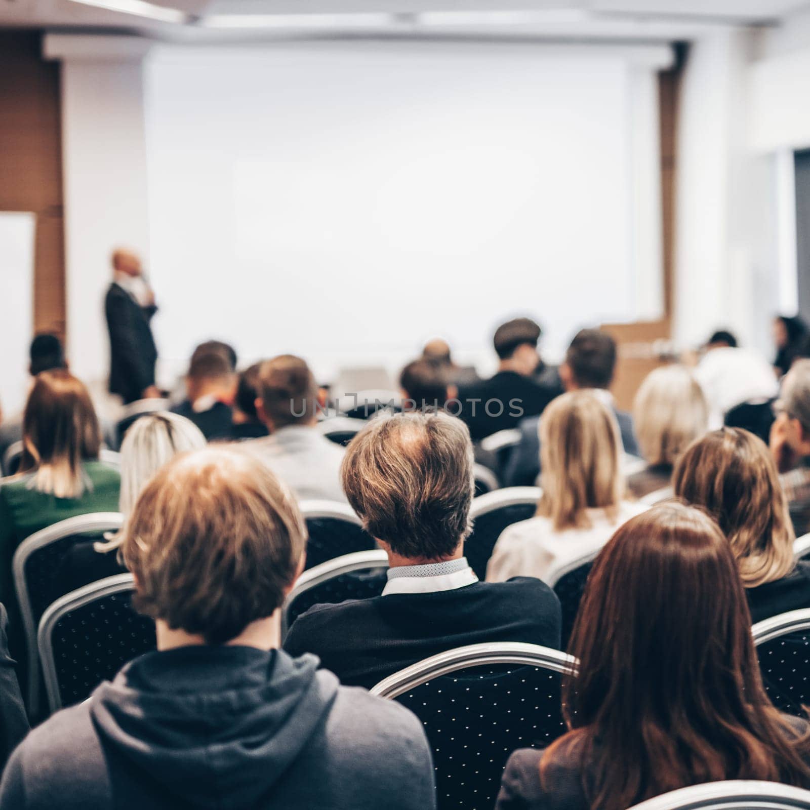 Speaker giving a talk in conference hall at business event. Rear view of unrecognizable people in audience at the conference hall. Business and entrepreneurship concept