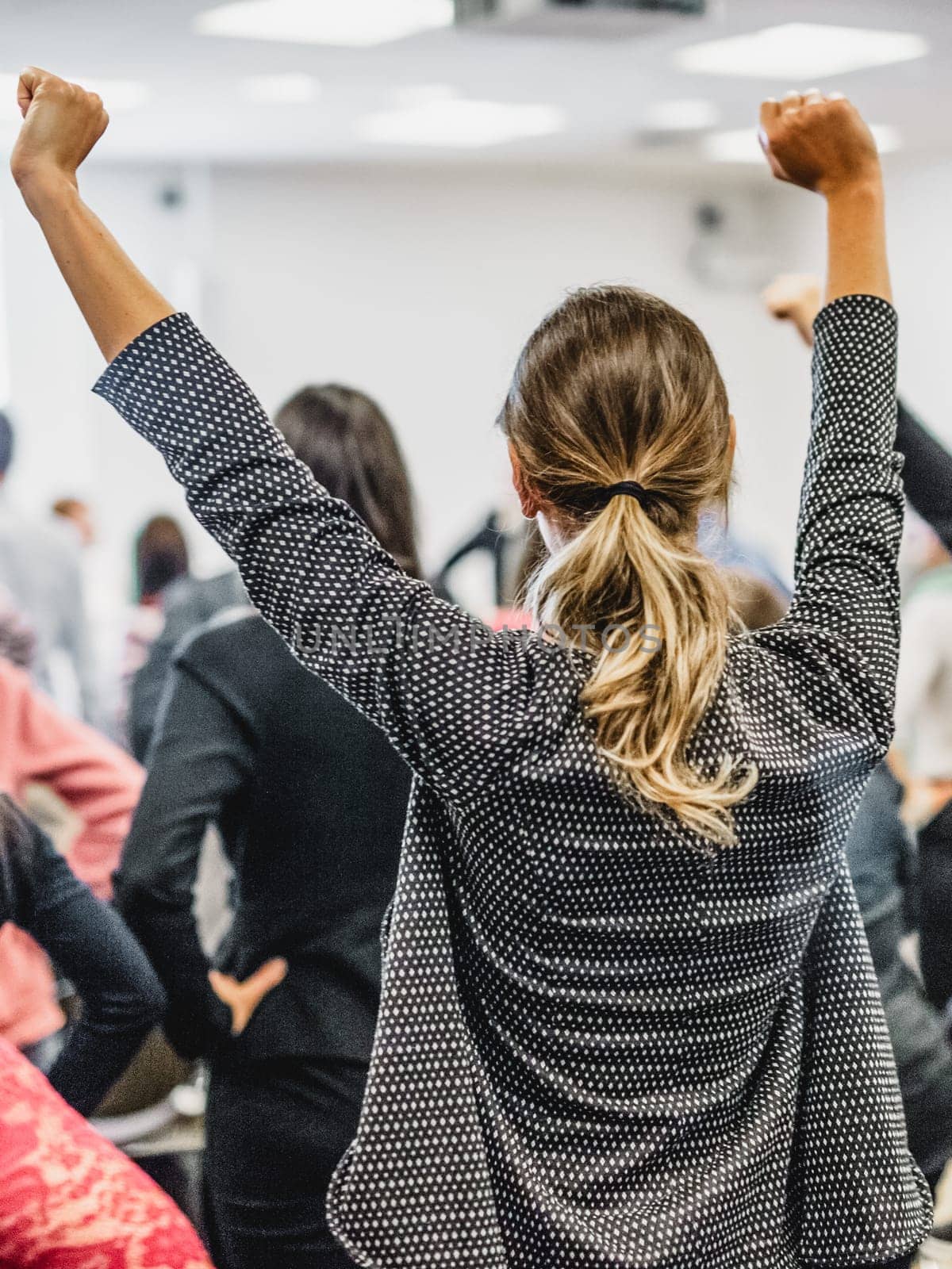 Life coaching symposium. Speaker giving interactive motivational speech at business workshop. Rear view of unrecognizable participants feeling empowered and motivated, hands raised high in air.