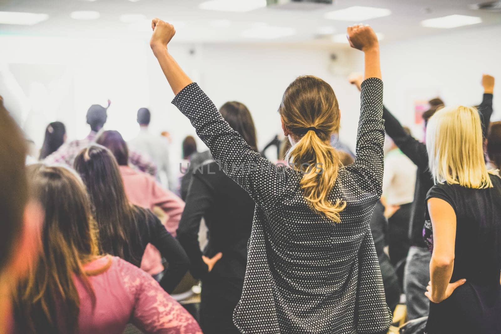 Life coaching symposium. Speaker giving interactive motivational speech at business workshop. Rear view of unrecognizable participants feeling empowered and motivated, hands raised high in air.