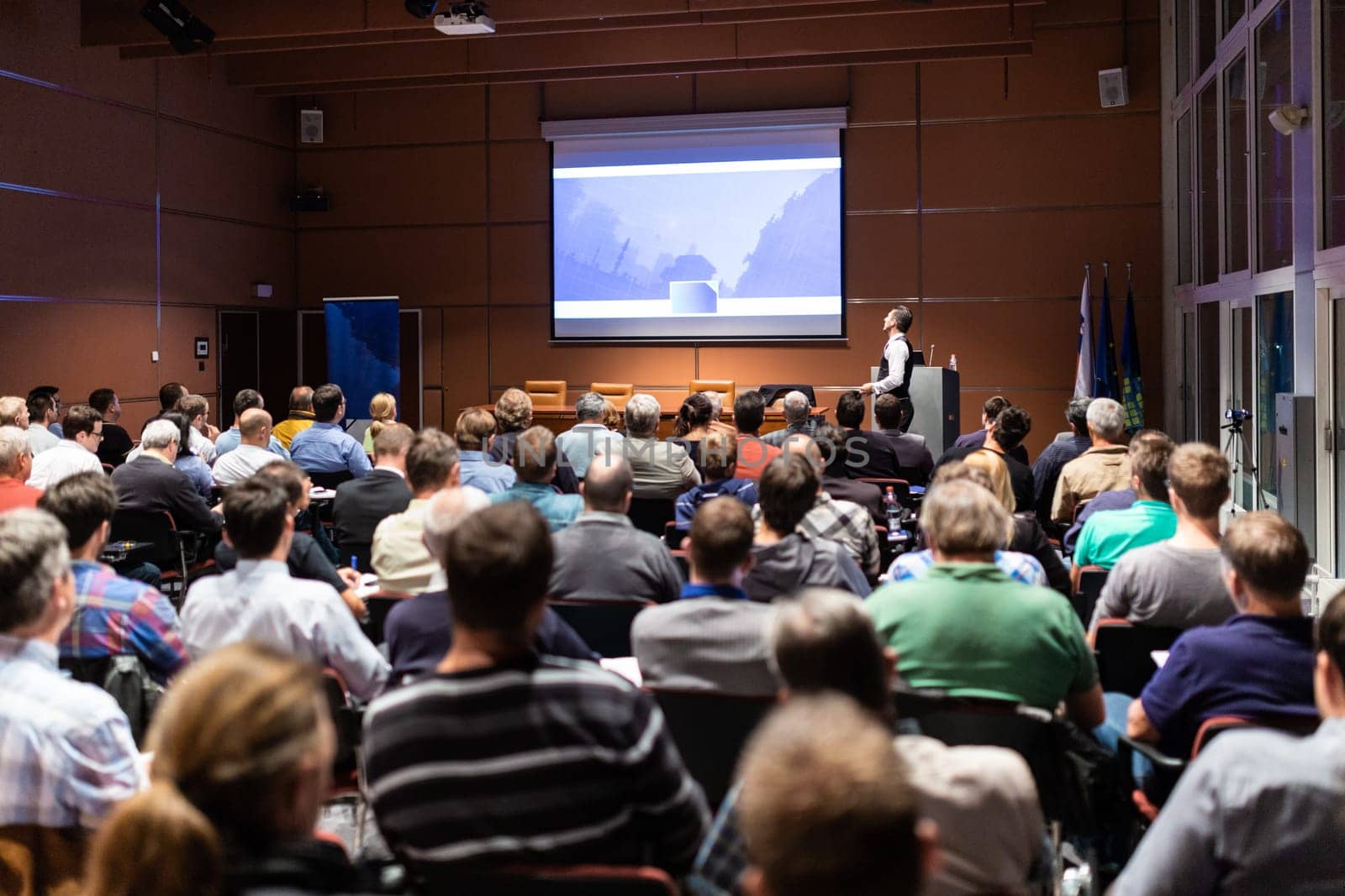 Speaker giving a talk in conference hall at business meeting event. Rear view of unrecognizable people in audience at the conference hall. Business and entrepreneurship concept.