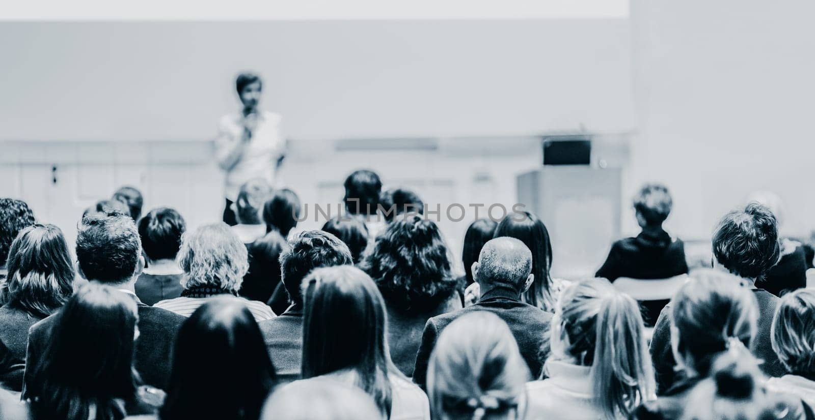 Female speaker giving presentation in lecture hall at university workshop. Audience in the conference hall. Rear view of unrecognized participant in audience. Scientific conference event.