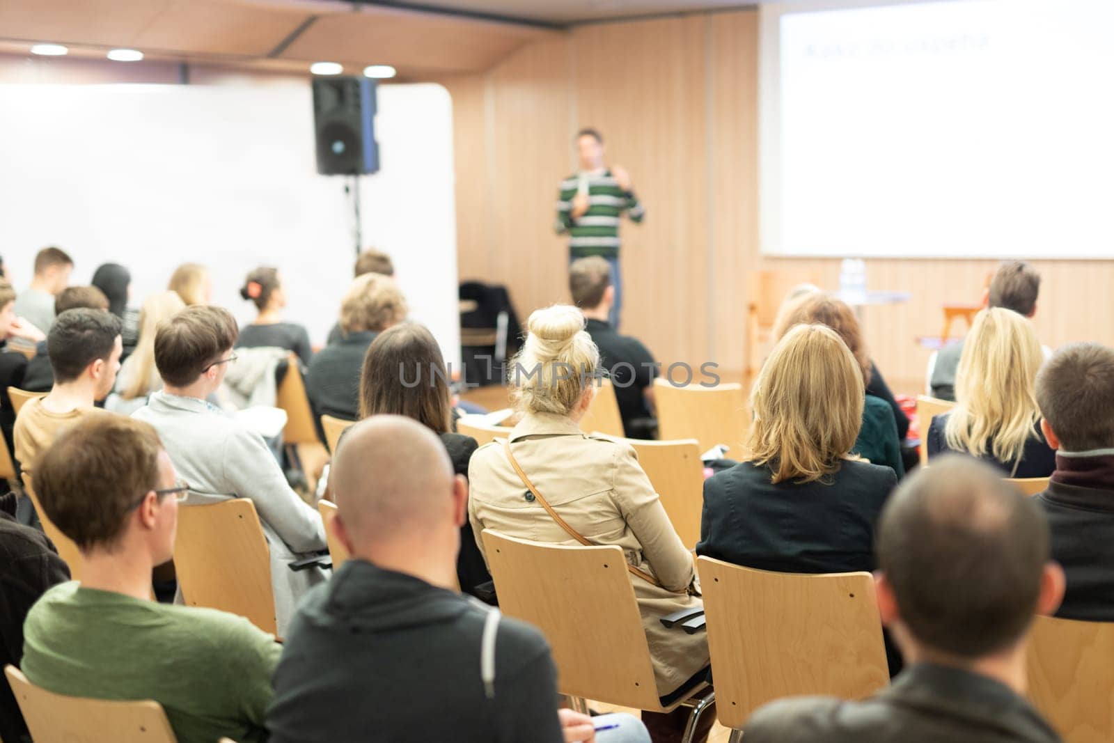 Business and entrepreneurship symposium. Female speaker giving a talk at business meeting. Audience in conference hall. Rear view of unrecognized participant in audience.
