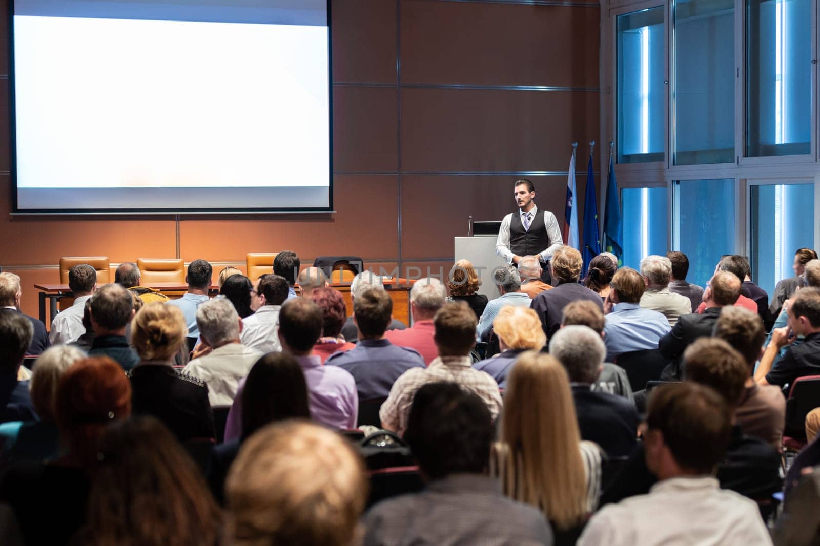 Speaker giving a talk in conference hall at business meeting event. Rear view of unrecognizable people in audience at the conference hall. Business and entrepreneurship concept.