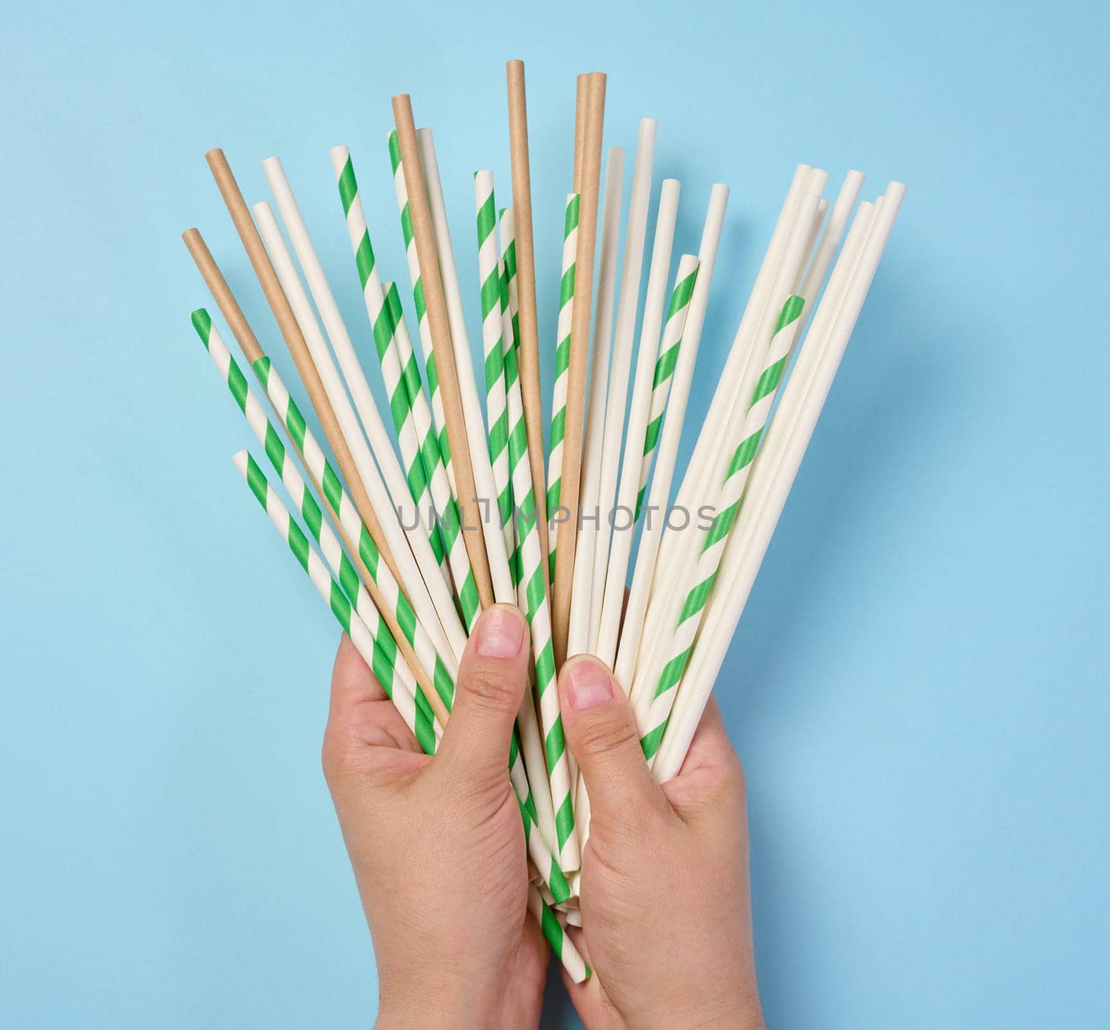Female hand holding paper cocktail straws on a blue background