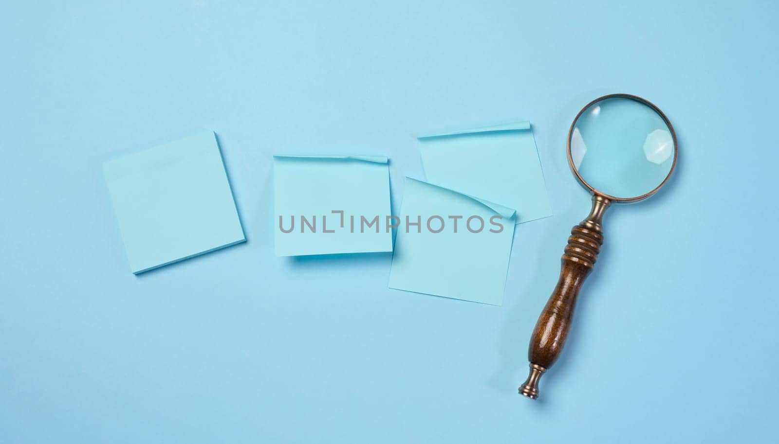Wooden magnifying glass and paper blue stickers on a blue background