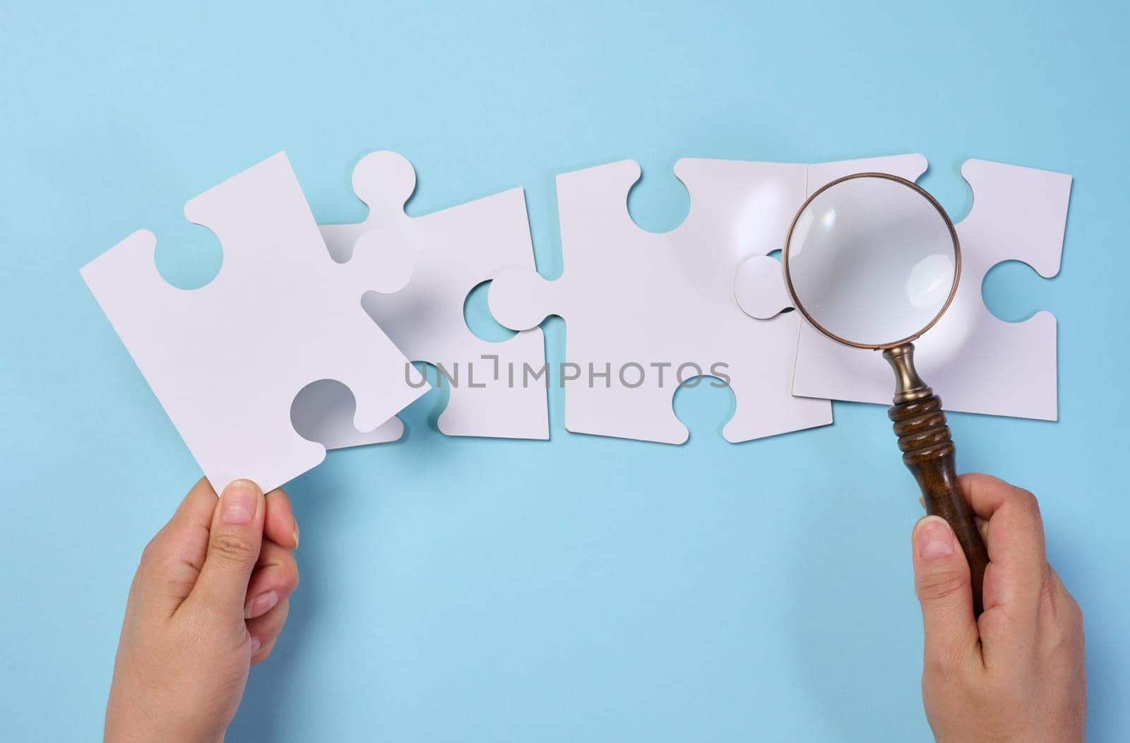 White empty puzzles and a magnifying glass in hand on a blue background, top view
