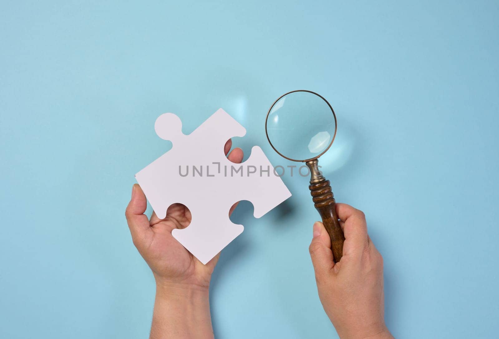 White empty puzzle and a magnifying glass in hand on a blue background, top view