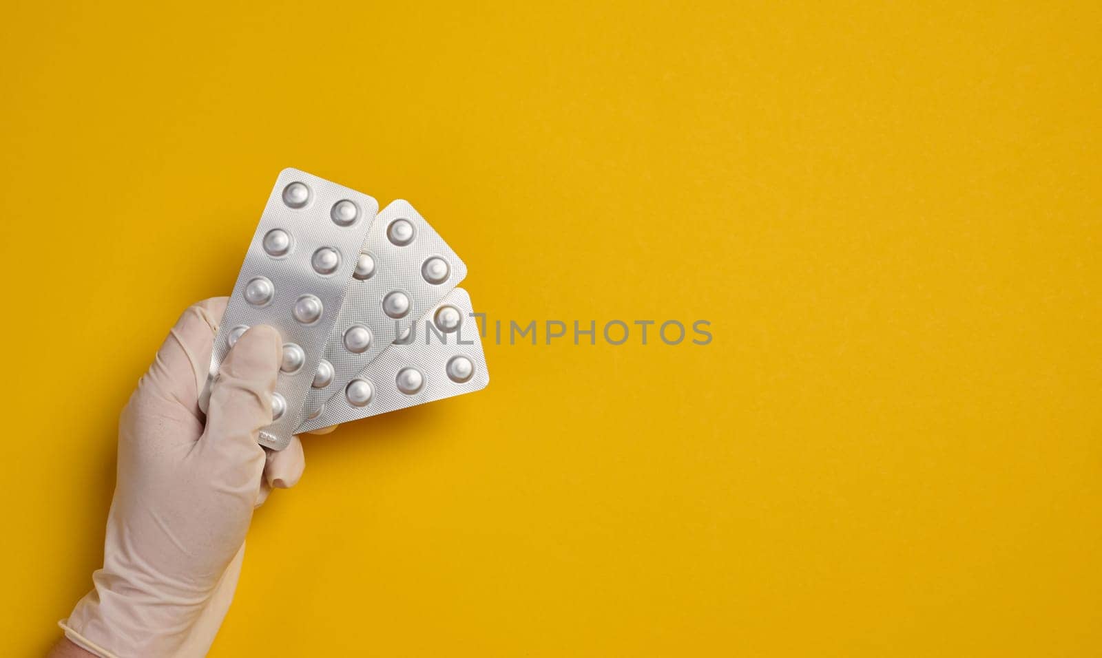 Female hand holding round pills in a blister pack on a yellow background, top view. Copy space
