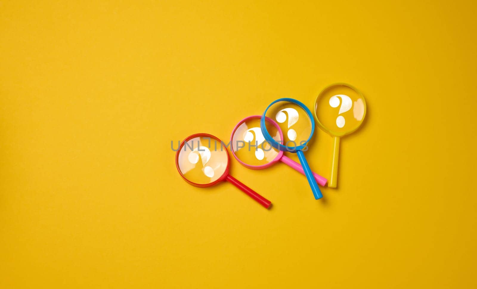 Plastic multi-colored magnifying glasses with a question mark on a yellow background, top view