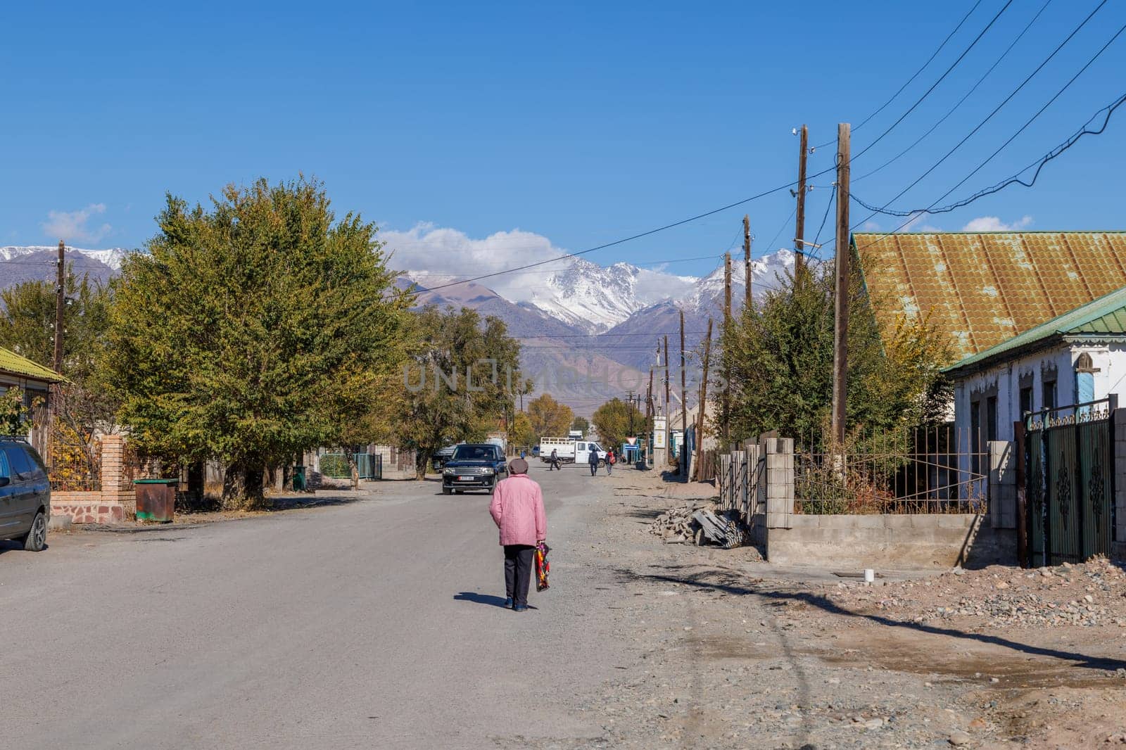 senior woman walking down the street of small Kyrgyz town at sunny autumn day in Balykchy, Kyrgyzstan- October 21, 2022