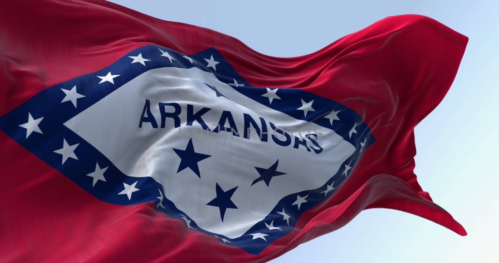 Arkansas state flag waving in the wind on a clear day. Red field with blue-bordered white diamond. 29 stars and ARKANSAS in blue. 3d illustration render. Selective focus. Fluttering fabric.