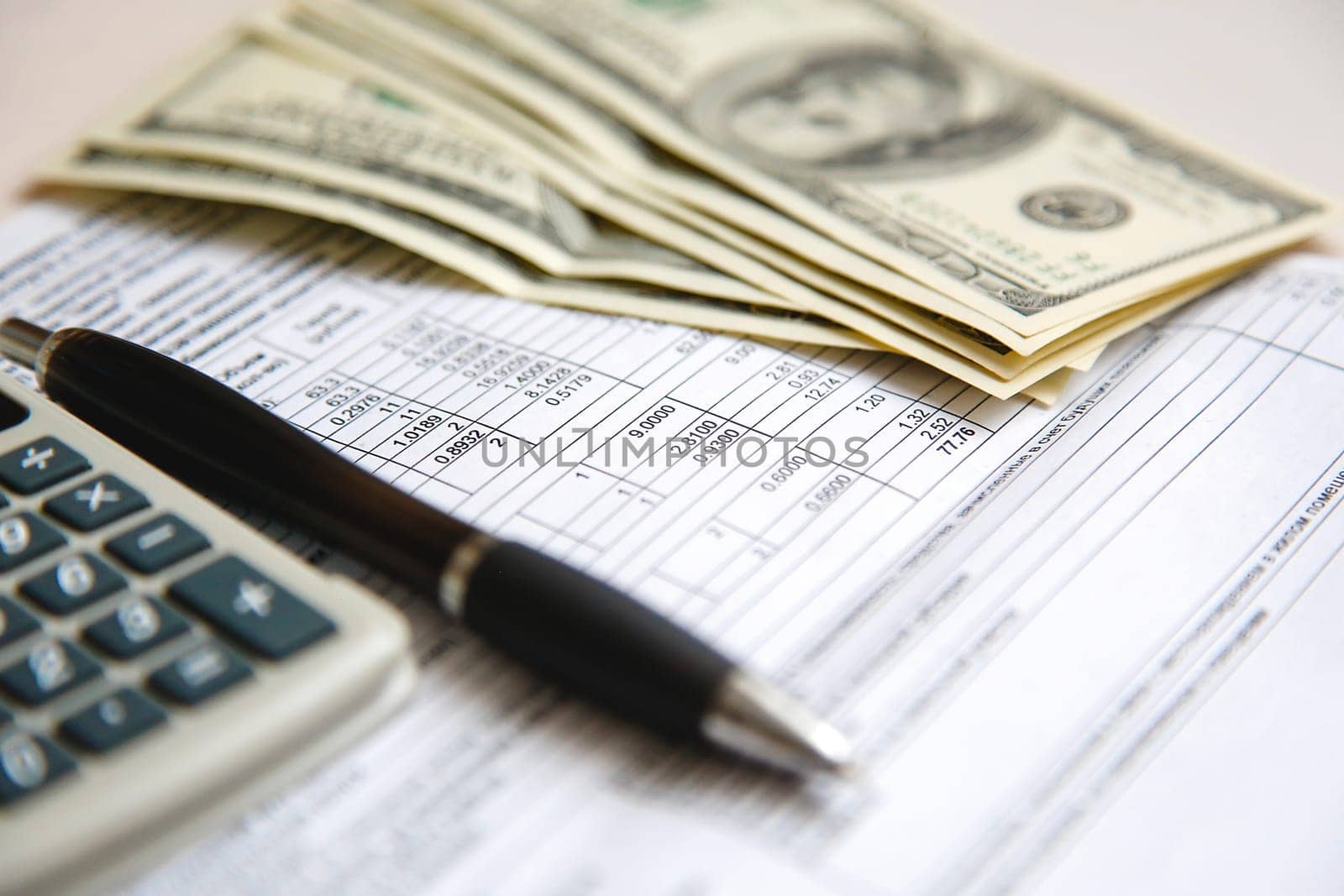 There are hundred dollar bills, a pocket calculator and a ballpoint pen on the settlement financial sheet of paper