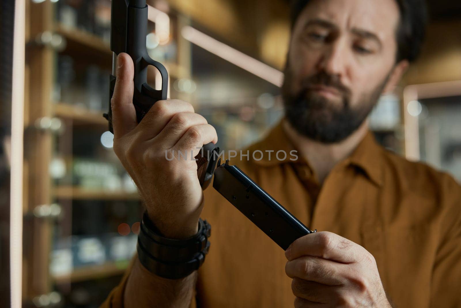 Portrait of salesman charging handgun demonstrating new model for customer standing over shop store showcase
