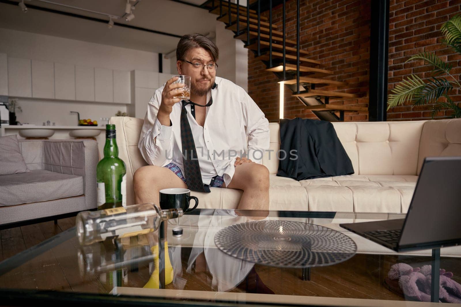 Frustrated drunk businessman working online having troubles with alcohol. Male boss entrepreneur discussing digital project remotely during virtual business meeting. Career and alcoholism