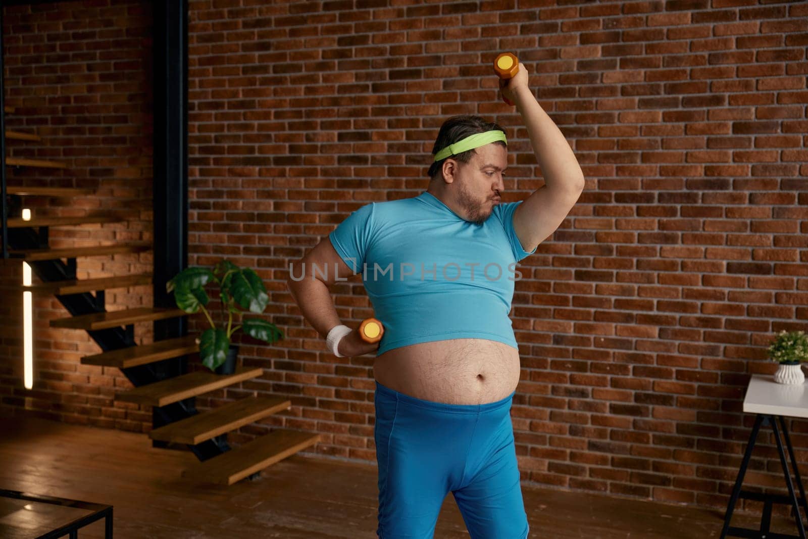 Fat man doing sport training with dumbbells at home. Funny hardworking guy exercising burning calories